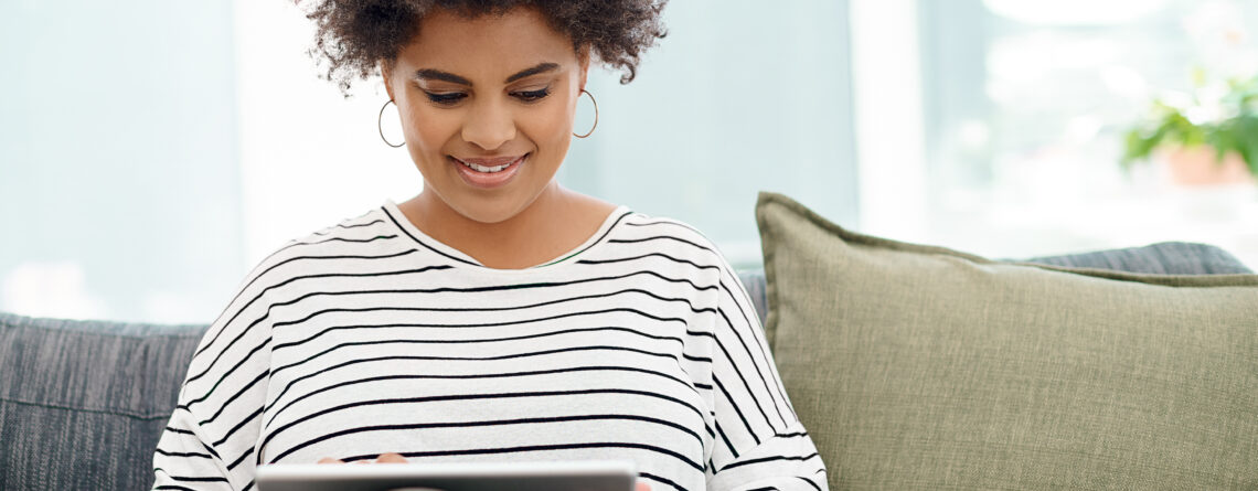 Person using a tablet for an online therapy session while sitting on a couch in a naturally lit room.