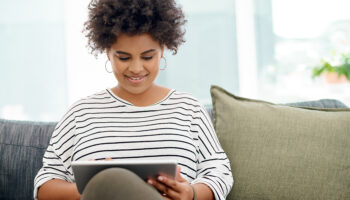 Person using a tablet for an online therapy session while sitting on a couch in a naturally lit room.