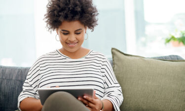 Person using a tablet for an online therapy session while sitting on a couch in a naturally lit room.