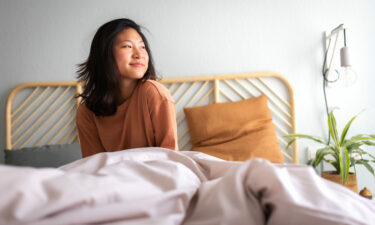 Happy young asian woman sitting on bed after waking up in the morning in beautiful, cozy bedroom at home after CBT-I treatment