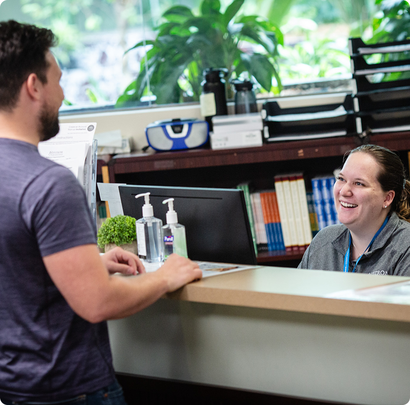 payment_process Smiling man speaking to a woman behind a counter in a friendly conversation.