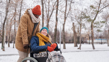 African American man talking to his friend in wheelchair during their walking in the park