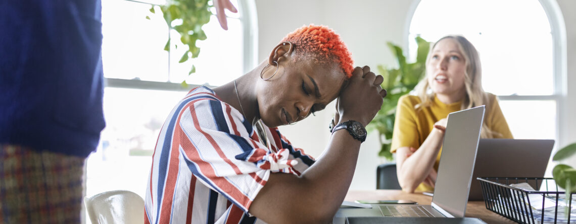 An African-American woman sitting in a conference room experiencing workplace anxiety